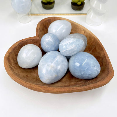 angled view of many blue calcite polished eggs in a heart bowl for possible variations