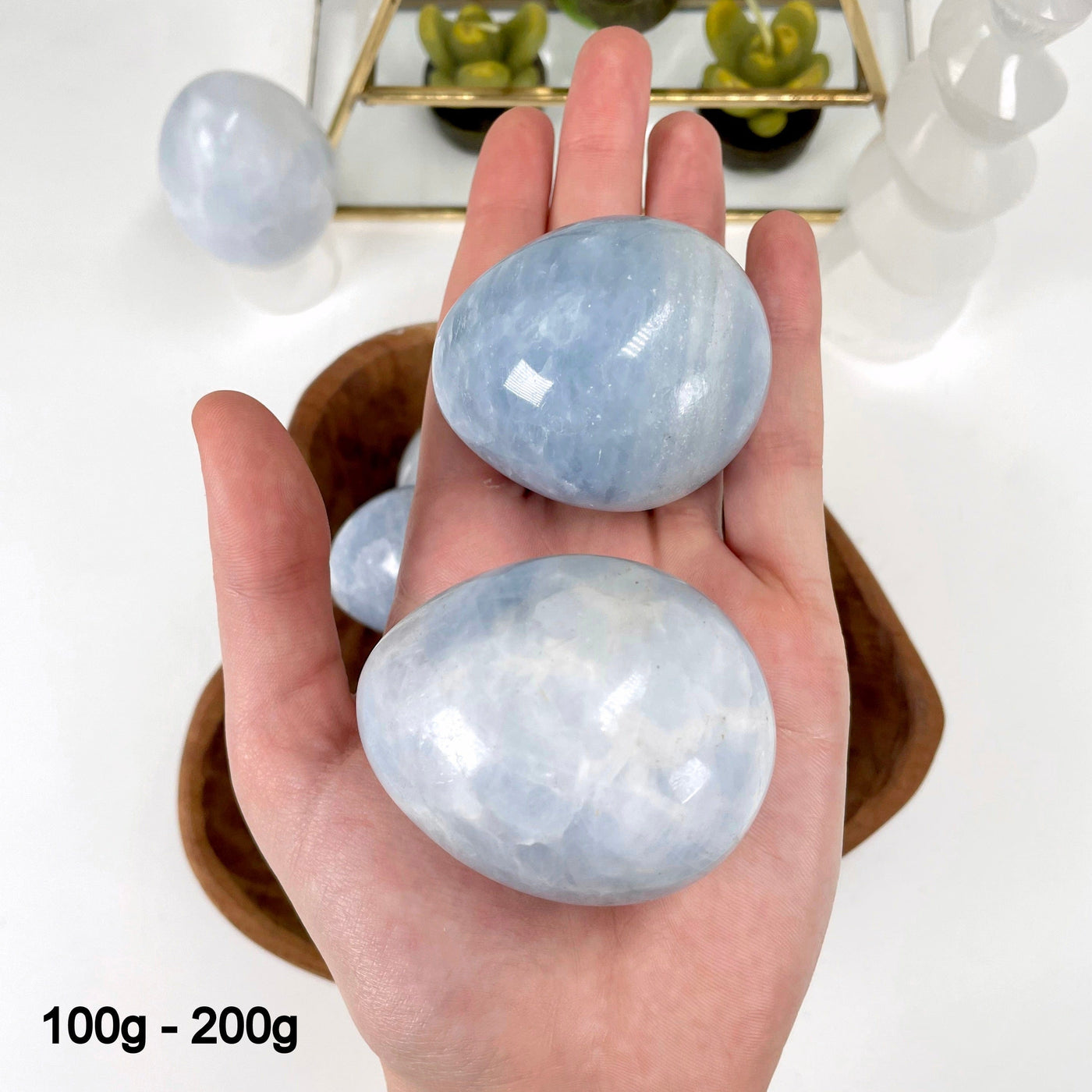 two 100g - 200g blue calcite polished eggs in hand for size reference and possible variations