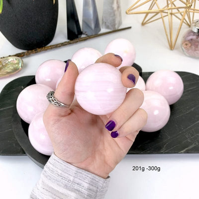 201 gram - 300 gram pink calcite sphere in hand with white background