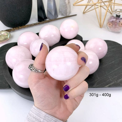 301 gram - 400 gram pink calcite sphere in hand with white background