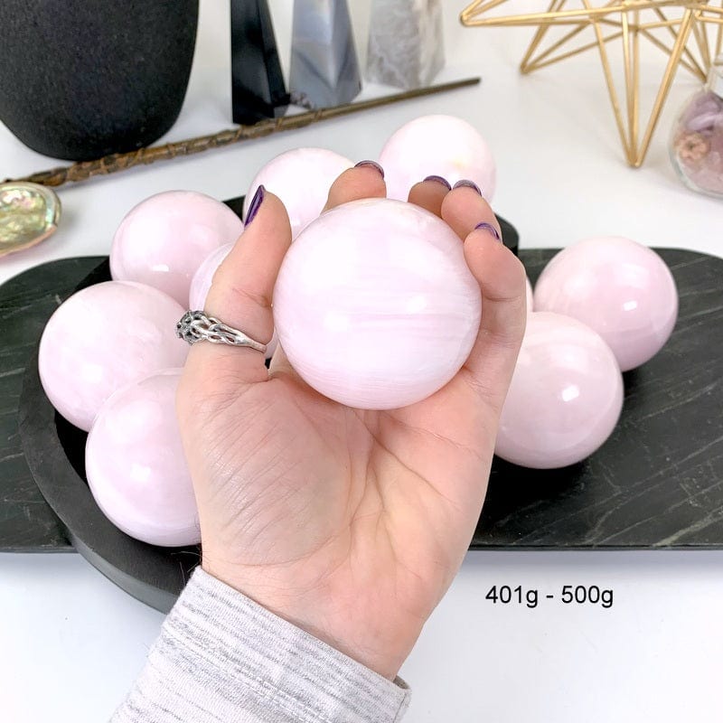 401 gram - 500 gram pink calcite sphere in hand with white background