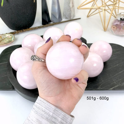 501 gram - 600 gram pink calcite sphere in hand with white background