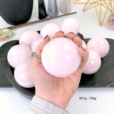 601 gram - 700 gram pink calcite sphere in hand with white background