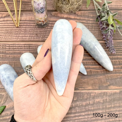 100 gram - 200 gram blue calcite wand in hand with wood background