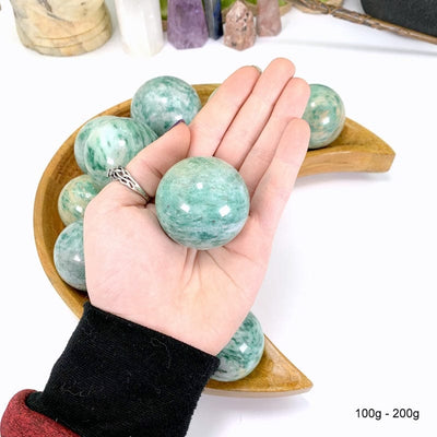 100 gram - 200 gram fuchsite sphere in hand with white background