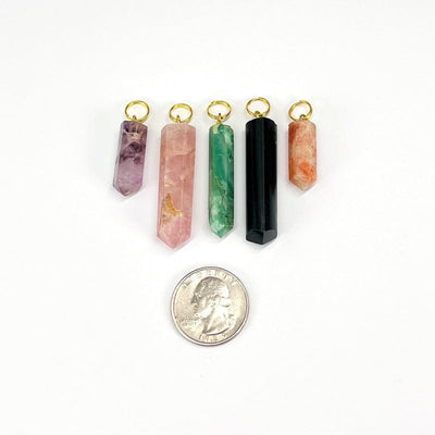 multiple pencil point gemstone pendants next to a quarter for size reference 