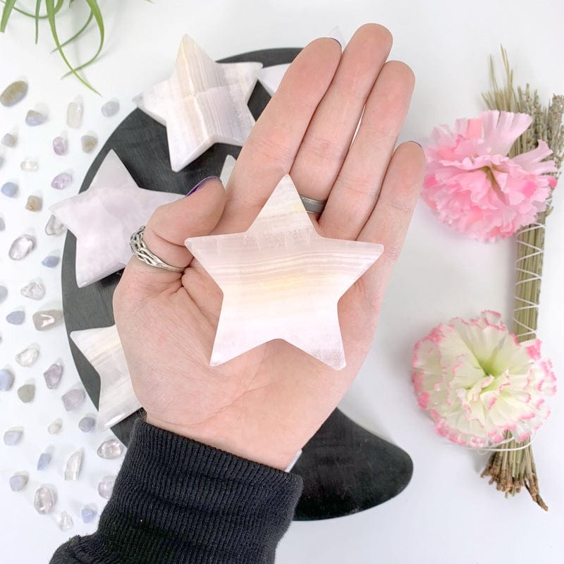 a single pink calcite star in hand above a white background