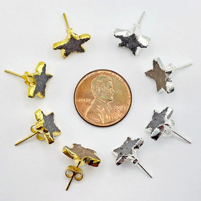 overhead view of four gold and four silver natural druzy star stud earrings surrounding a penny for size reference