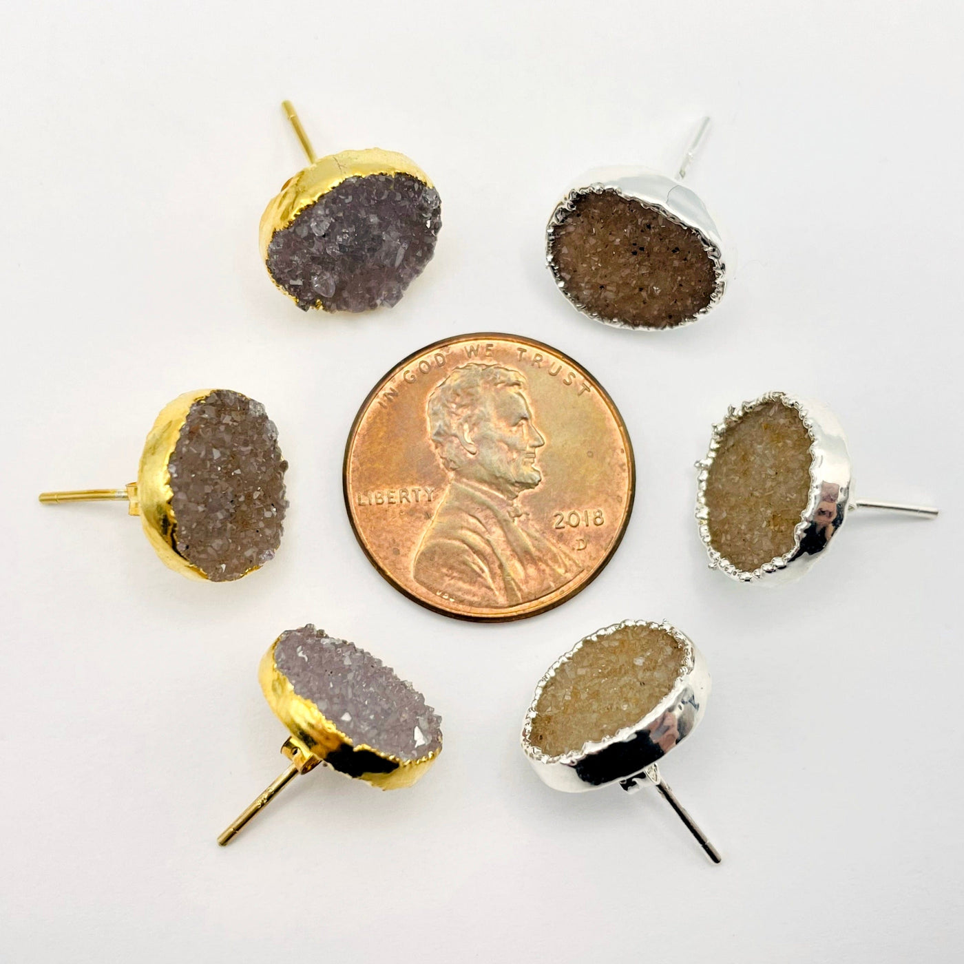 overhead view of three gold and three silver natural druzy round stud earrings surrounding a penny for size reference