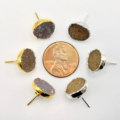 overhead view of three gold and three silver natural druzy round stud earrings surrounding a penny for size reference