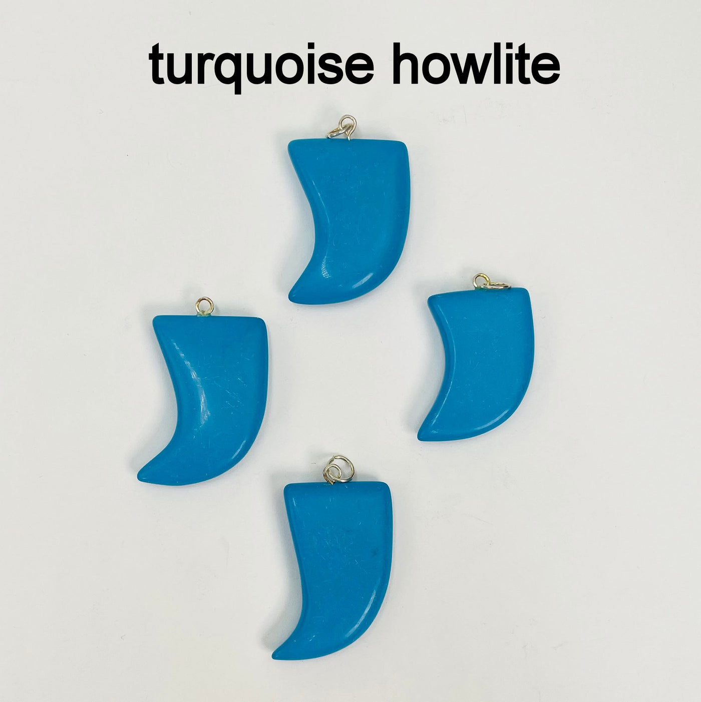 close up of four tumbled turquoise howlite horn pendants on white background for details and possible variations
