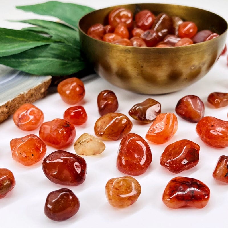 Carnelian stones on a white background with more in a brass bowl.