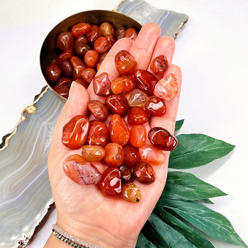 Orange Carnelian stones in the palm of a woman's hand with more in a bowl in the background.