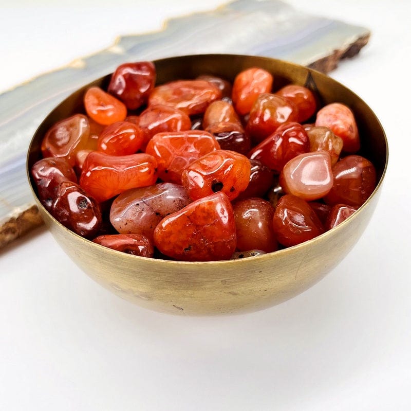 Carnelian tumbled stones in a brass bowl.