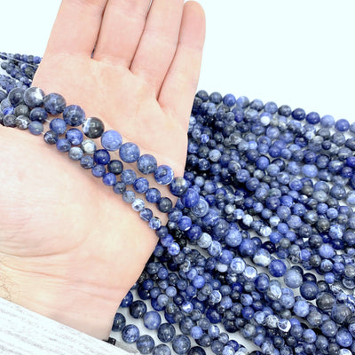 3 strands sitting on a hand in front of a lot more sodalite beads with a white background