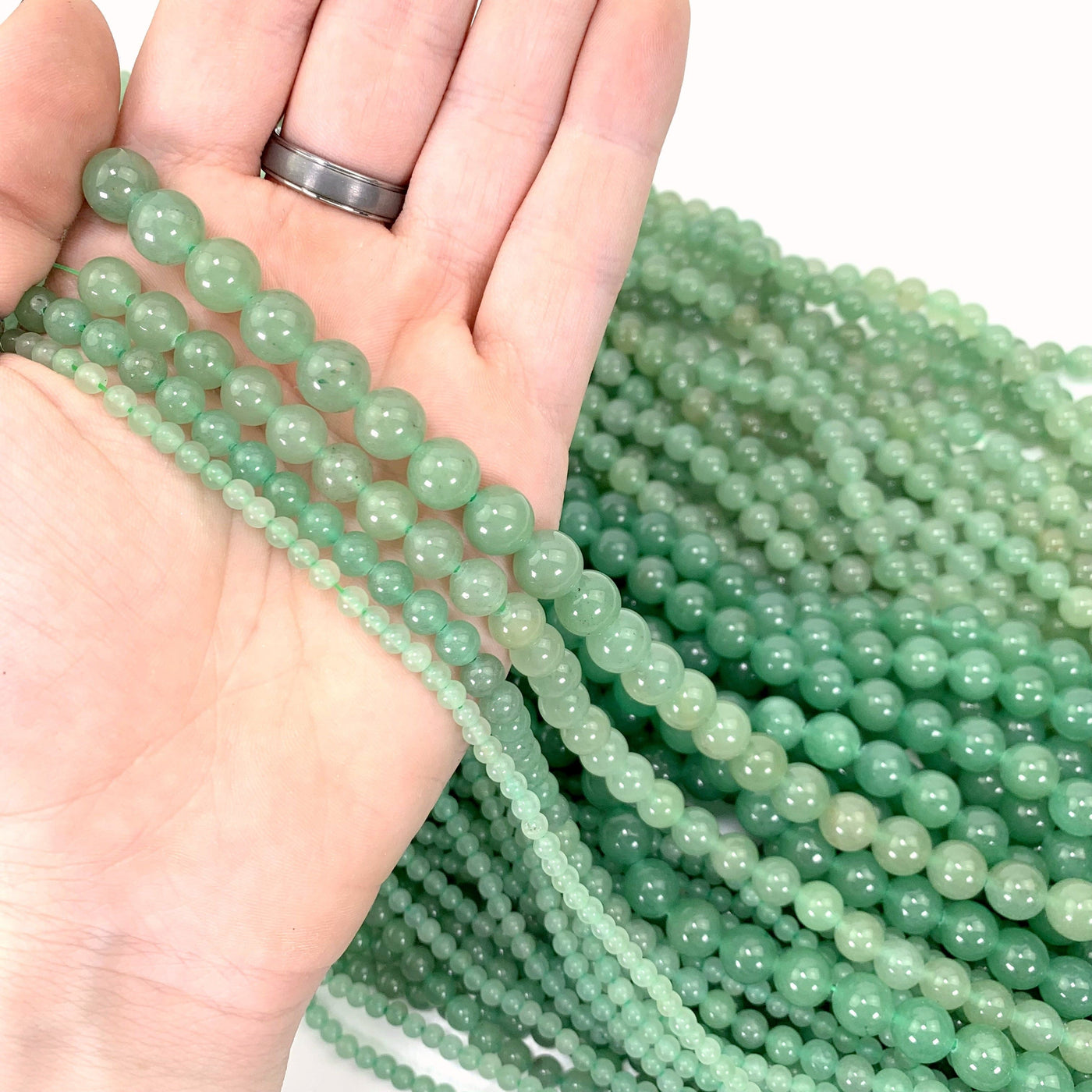 all 4 variations in hand with more green aventurine beads in background on a solid white background