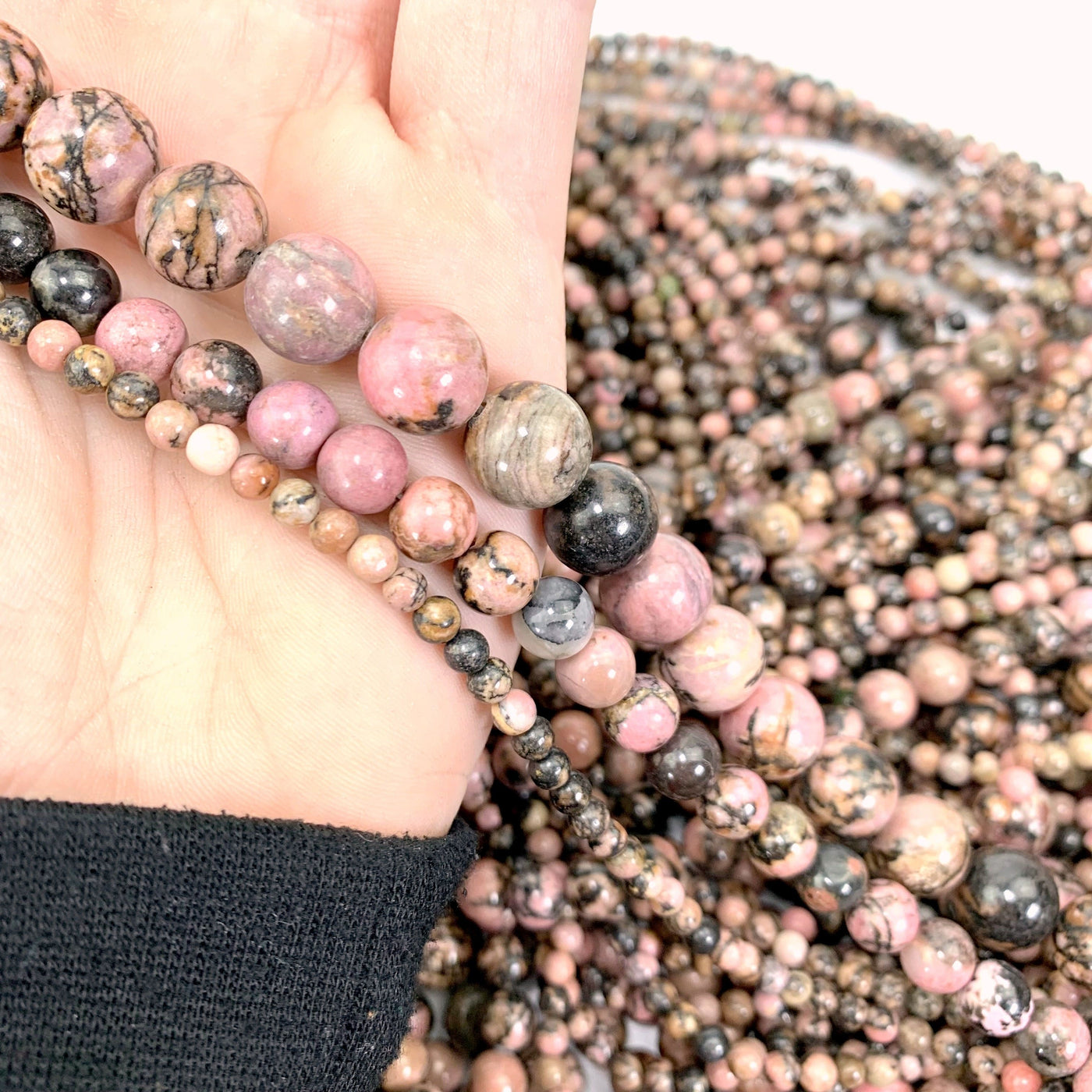 all 3 variations of rhodonite beads in hand with more rhodonite beads in background