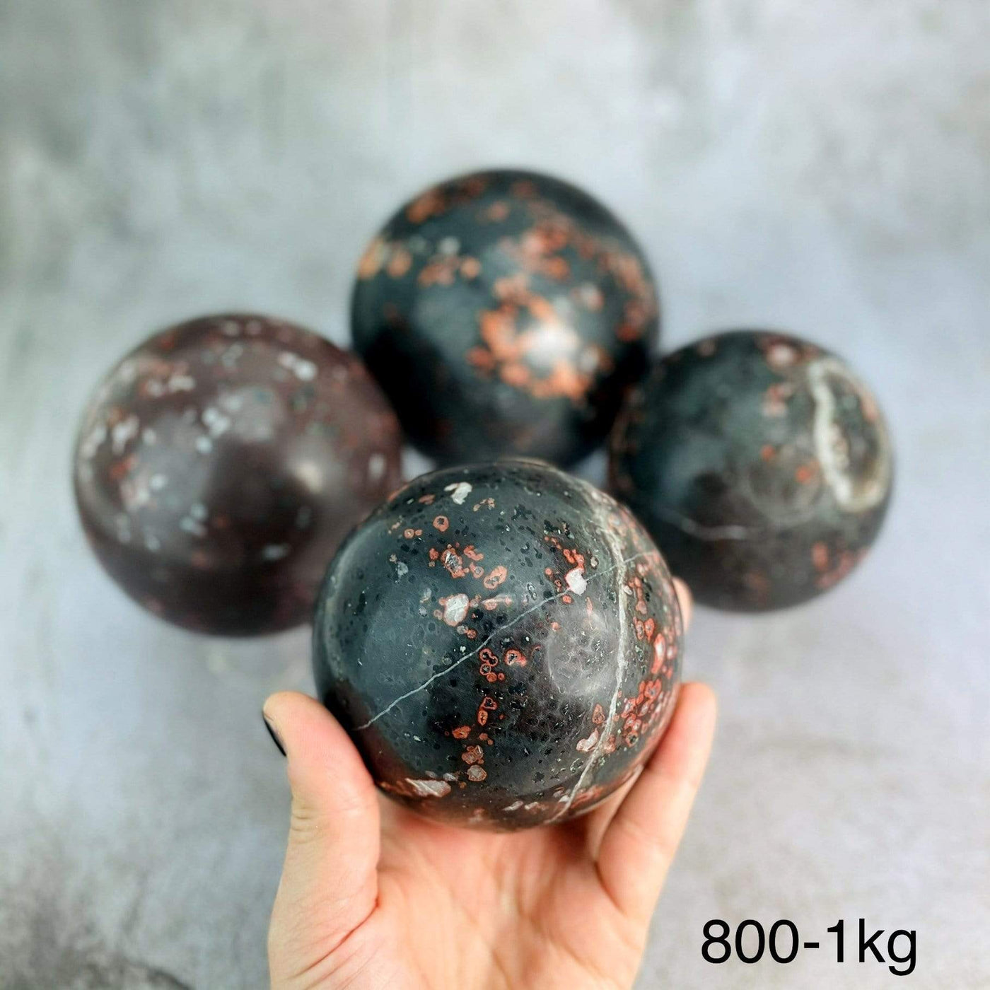 hand holding up 800-1kg plum blossom jasper stone sphere with other blurred in the background