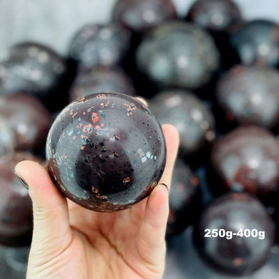 hand holding up 250g-400g plum blossom jasper stone sphere with other blurred in the background