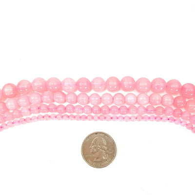 photo of all four sizes of round rose quartz beads on a white background with a quarter for sizing reference