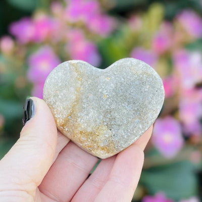 Front facing Druzy Natural Agate Heart Shaped Stone in a hand. Flowers are in the background.