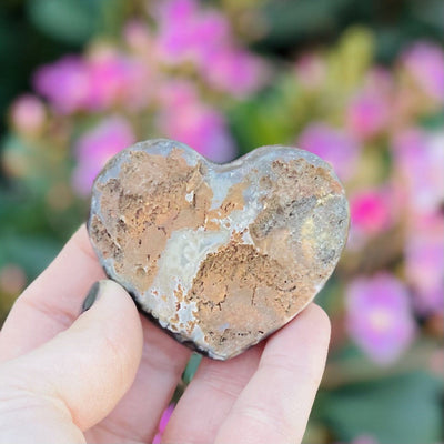 Back view of Druzy Natural Agate Heart Shaped Stone in a hand. Flowers are in a hand.