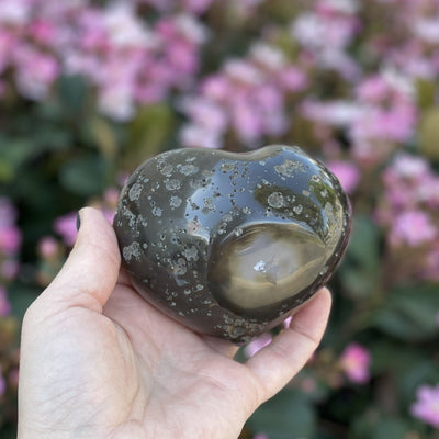 Backside of agate heart with druzy in a hand showing the polished external surface.
