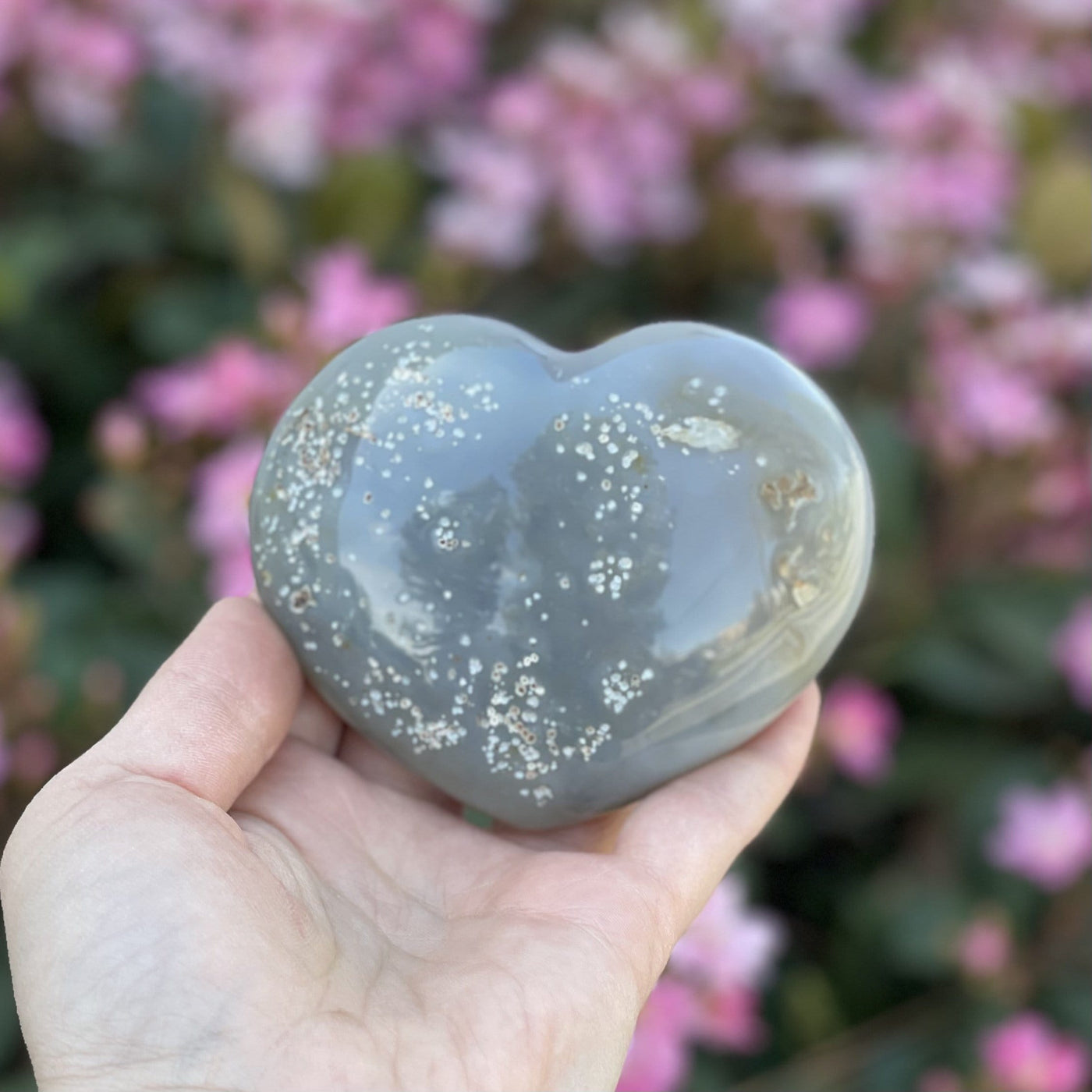 Back side of  Druzy Natural Agate Heart Shaped Stone in a hand with flowers in the background.