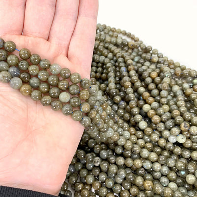 Dark Labradorite Beads In Hand With More Labradorite Beads In Background.