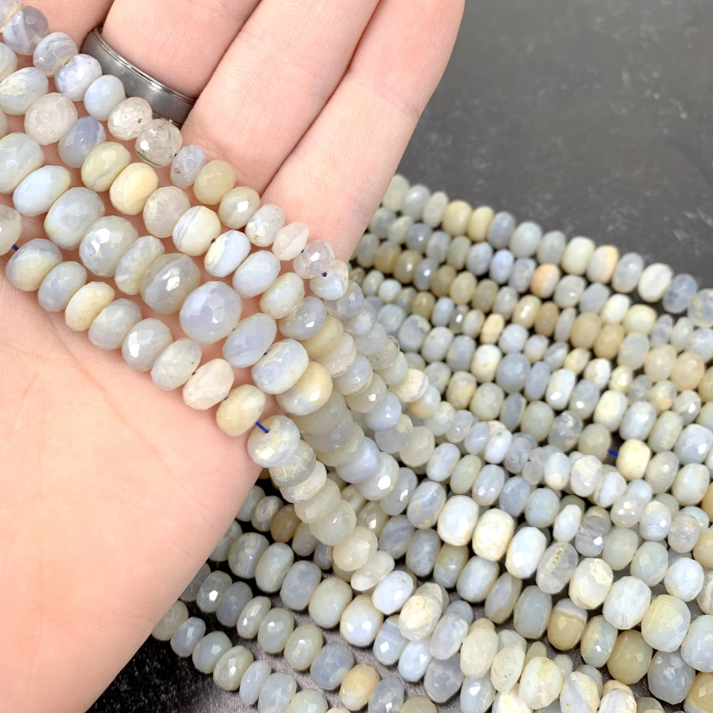 faceted round chalcedony beads in hand with more beads in background on black