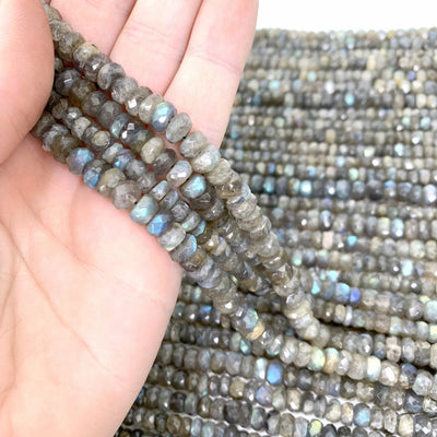 FACETED ROUND LABRADORITE BEADS in hand with mroe beads in the background on a white surface