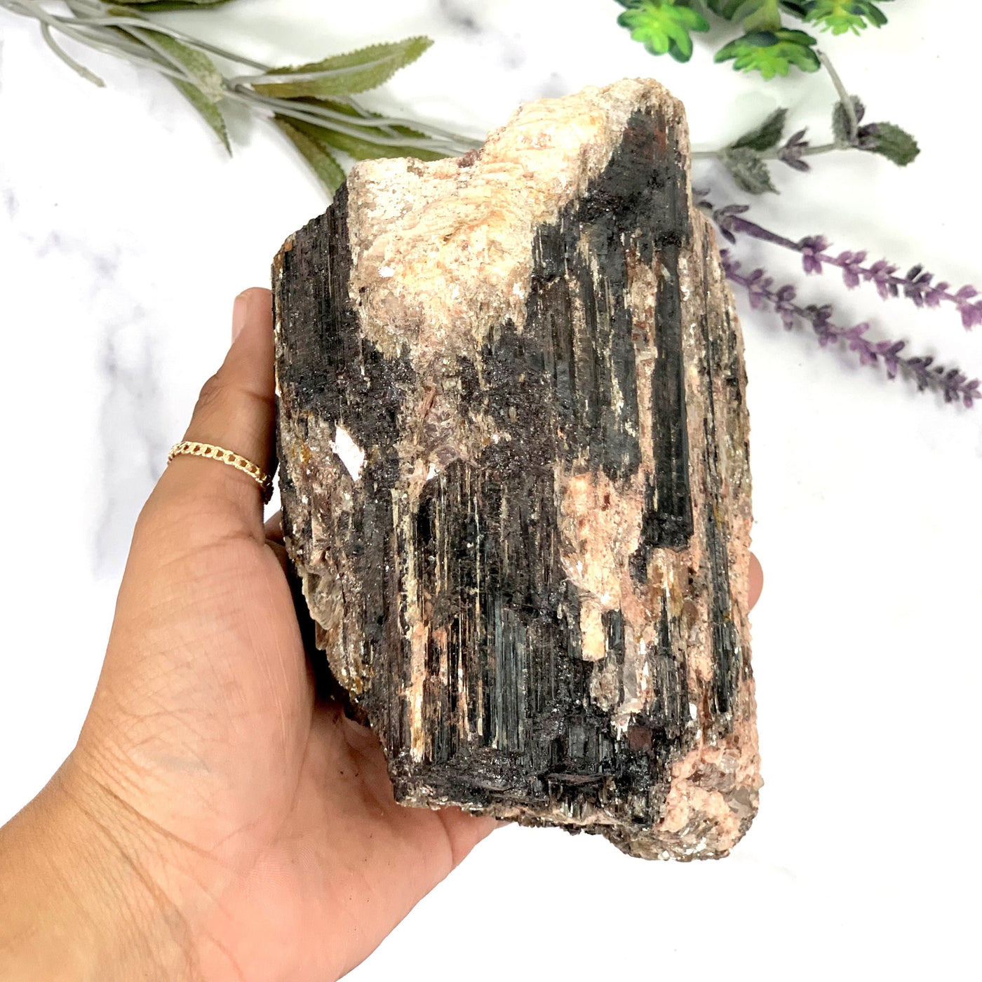 hand holding up Black Tourmaline with Mica on Matrix on marble background with plants