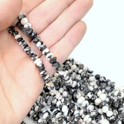 both variations of zebra jasper (left flat, right round) strands in hand with more beads in background on a white background