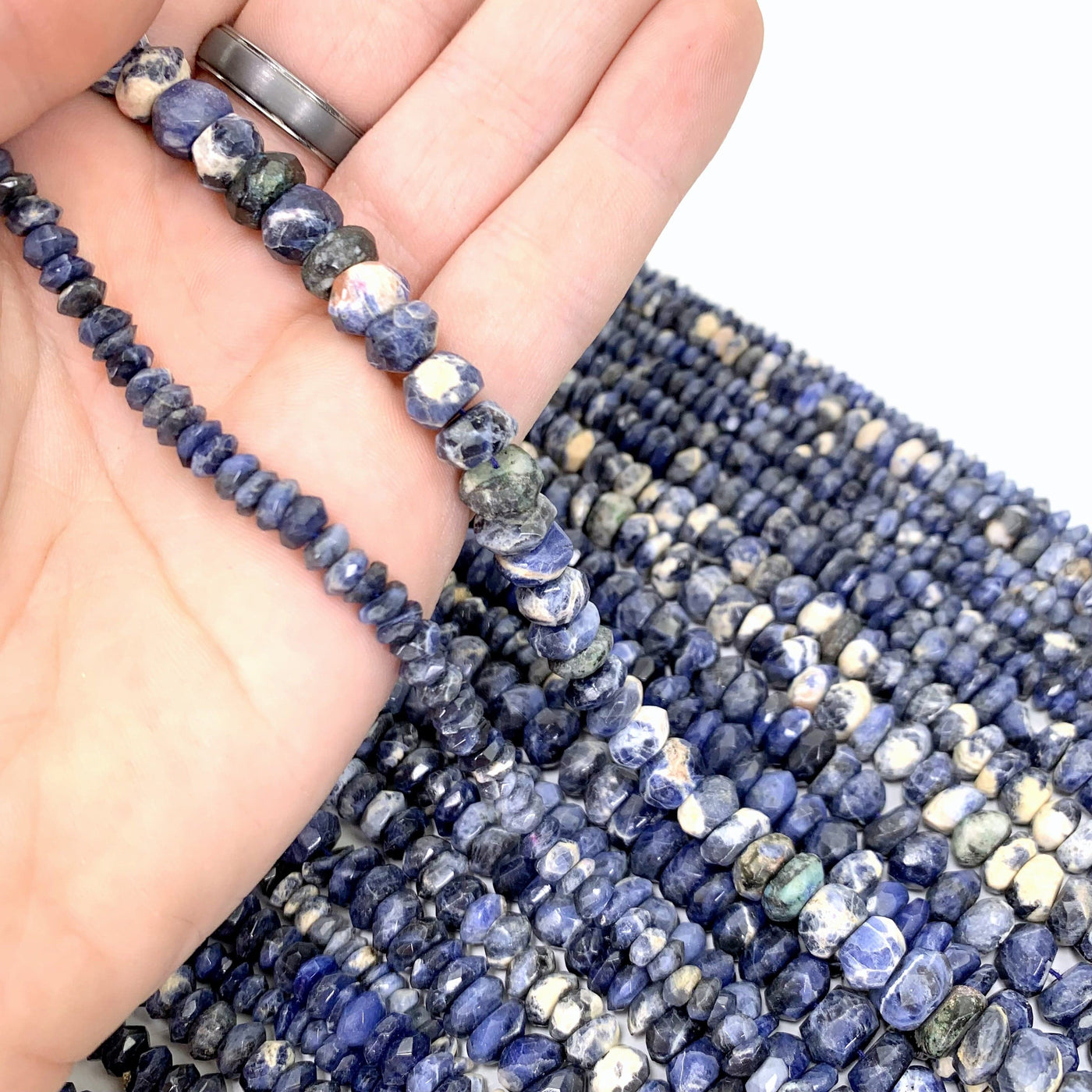 both sodalite variations ( small left, large right) in hand with more sodalite beads in the background on a white background