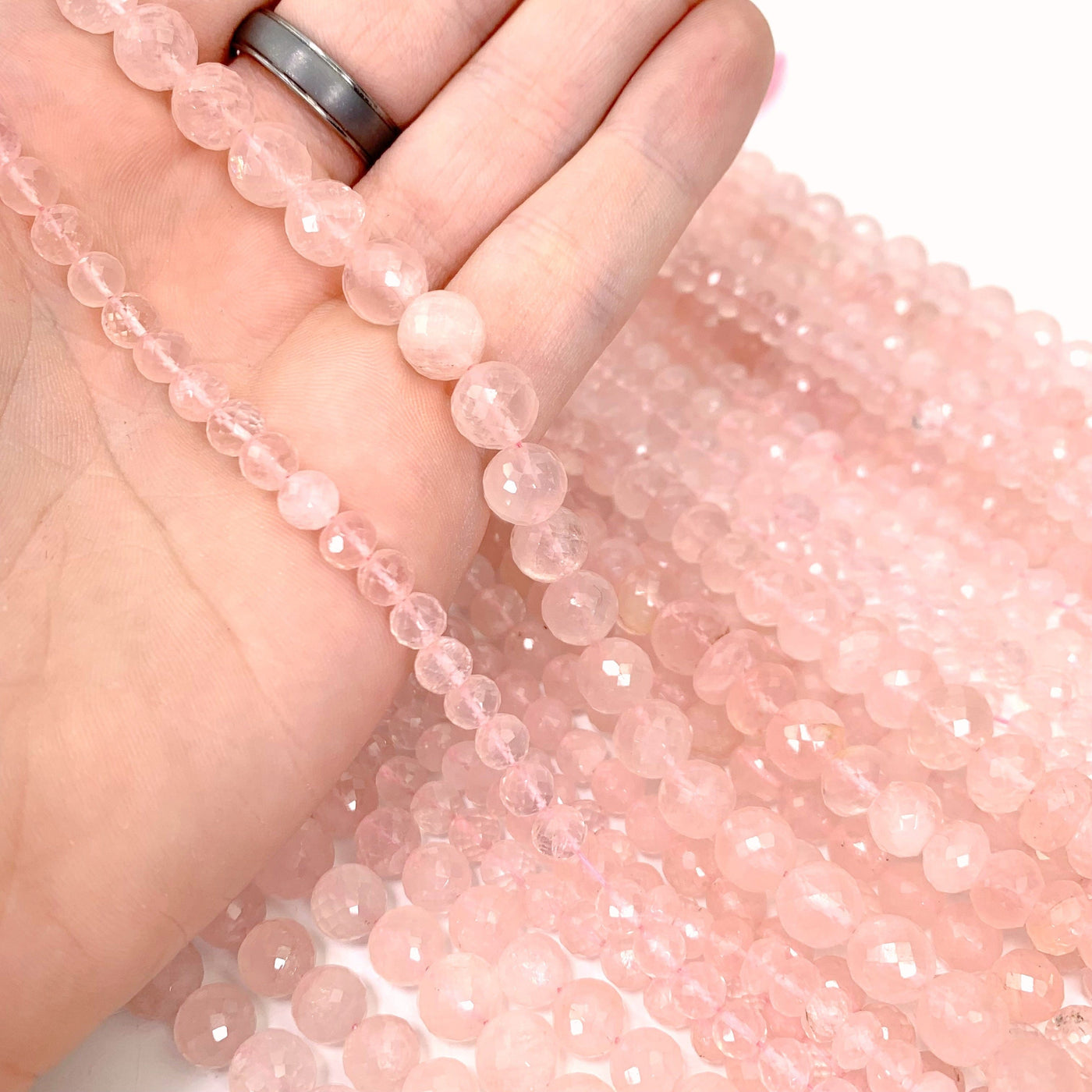 both variations of rose quartz (left small, Right large) strands in hand with more rose quartz beads in background with a white background