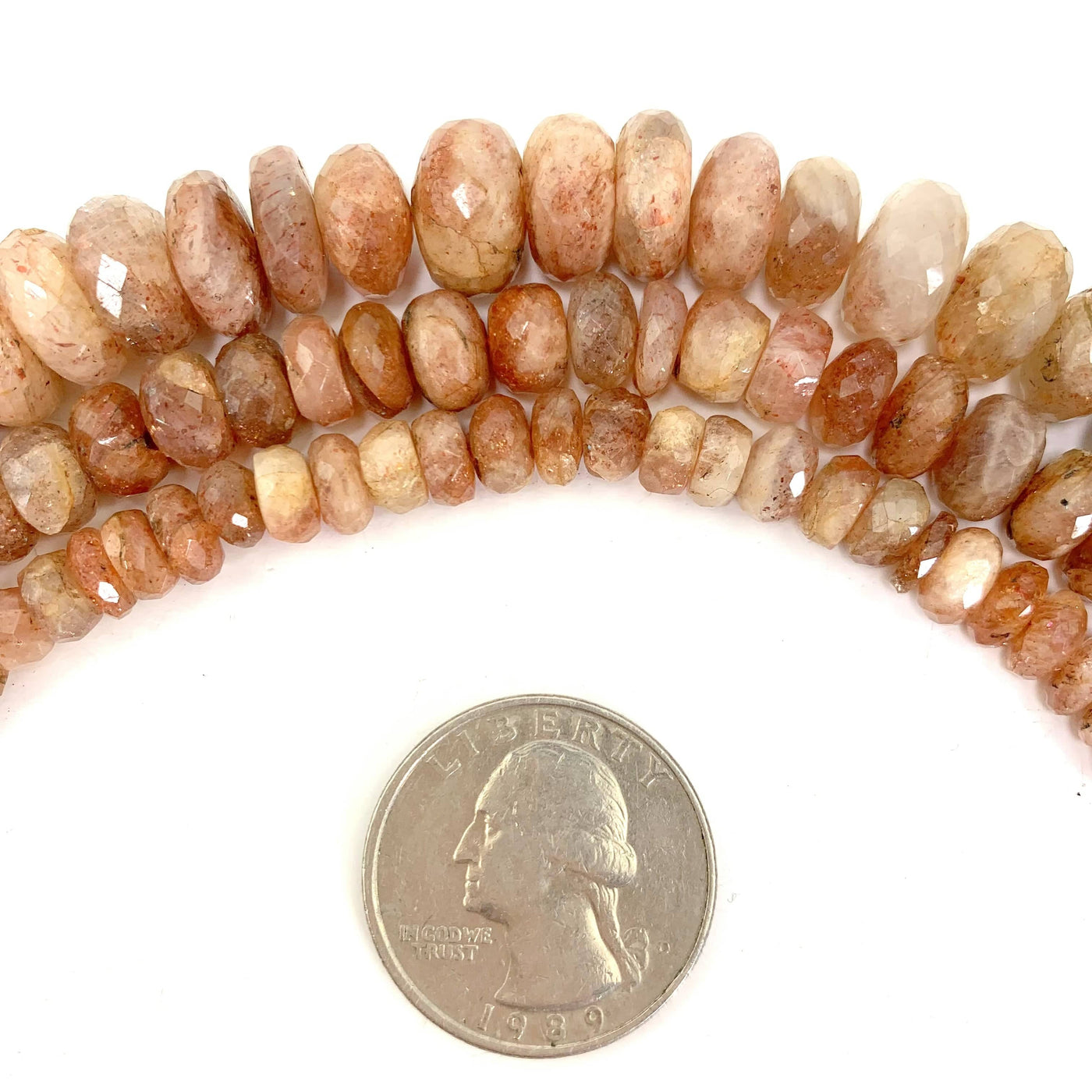 all 3 variations ( top large, middle medium, bottom small)  of sunstone faceted beads on a white background next to a quarter