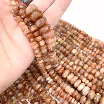 all 3 variations of sunstone faceted beads in hand (left small, middle medium, right large) with more sunstone beads in hand with a white background