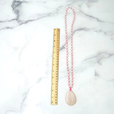 Top angle shot of ruler comparing size to the Rose Quartz Tear Drop Pendant on Beaded Mala Necklace