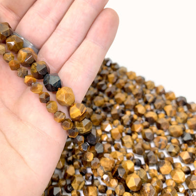 Faceted Pentadecagon Tiger Eye Beads in hand (left small, right large) with more tigere eye beads inh background on a white background