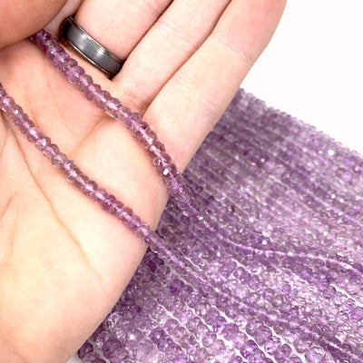 both amethyst bead strands in hand ( left small, right large) with more amethyst beads in the background on a white background