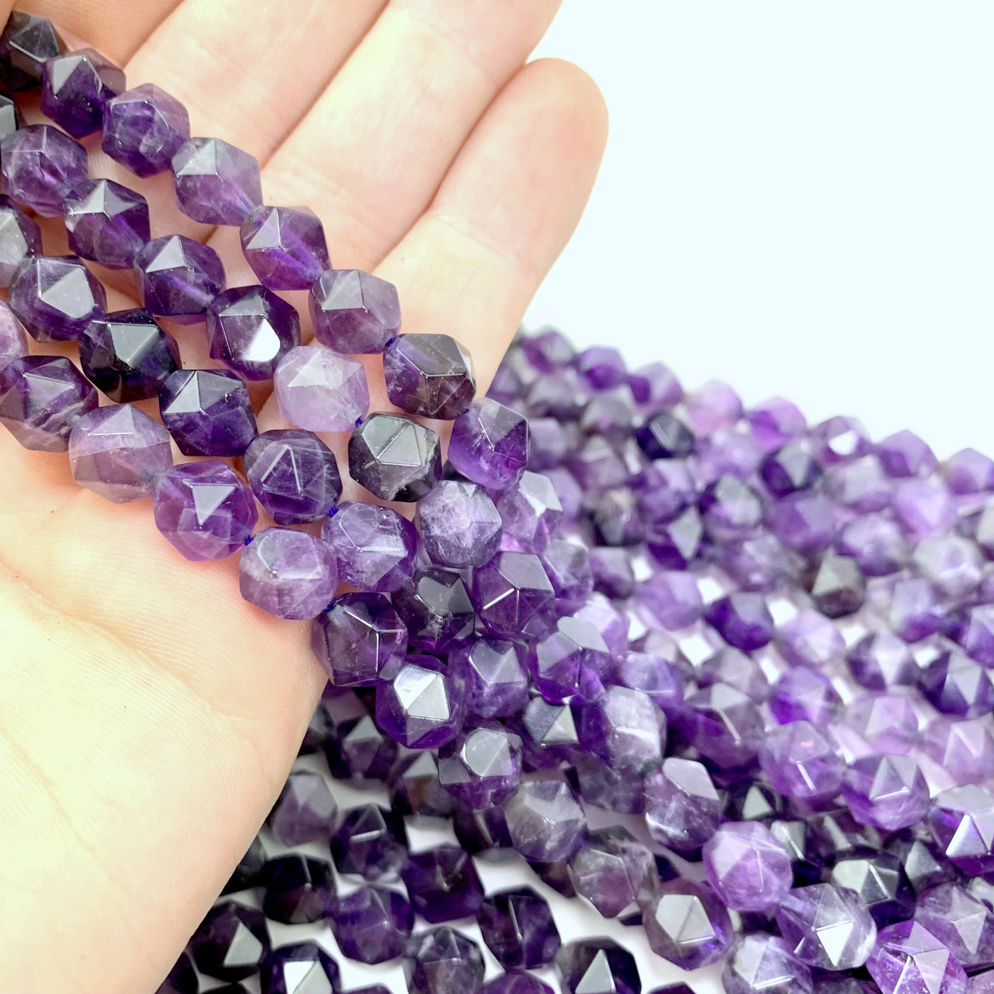 amethyst beads in hand with more amethyst beads in the background with a white backdrop
