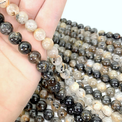 both light (right) and dark (left) rutilated beads in hand with more rutilated beads in the background with a white backdrop
