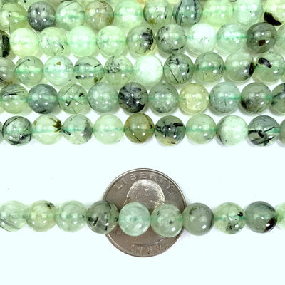 prehnite beads laid out on a white background with one strand laid over a quarter