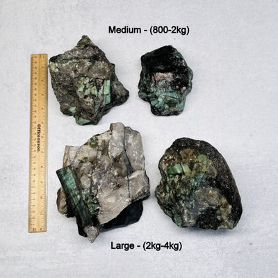raw emerald clusters next to a ruler for size reference. displayed is the medium and large clusters 