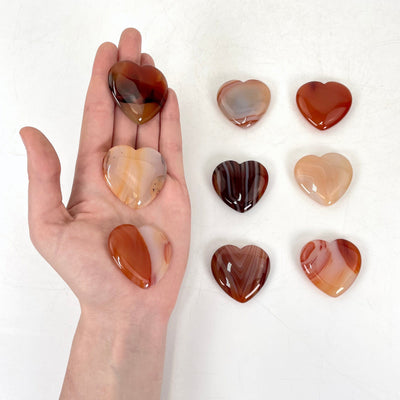 three carnelian polished hearts in hand for size reference