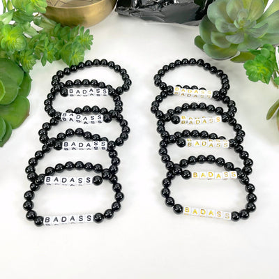 black "BADASS" letter beads on left display and gold "BADASS" letter beads on right display