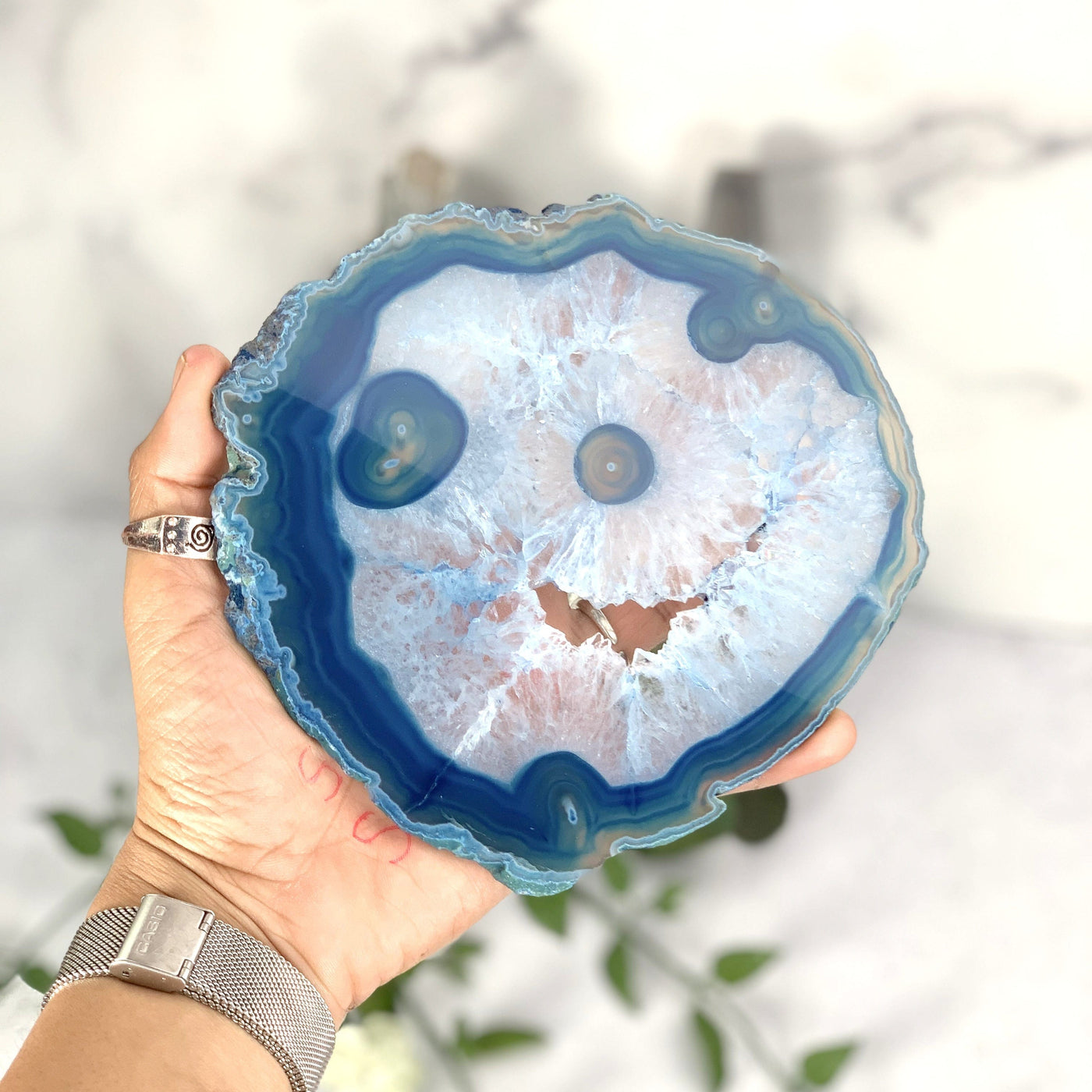 Hand holding the backside of the blue dyed agate slice with druzy