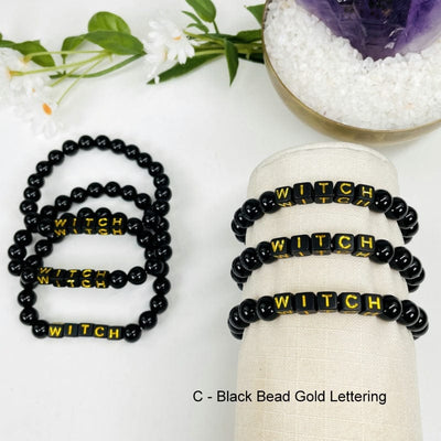 obsidian bracelet with black beads that spell out WITCH in gold letters