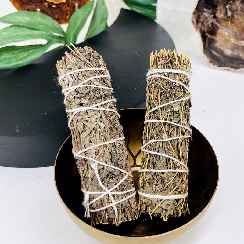 2 mugwort smudge bundles in a bowl with decorations in the background