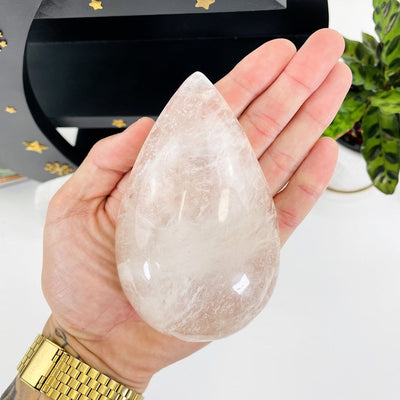 hand holding up Clear Quartz Tear Drop Shape with decorations in the background